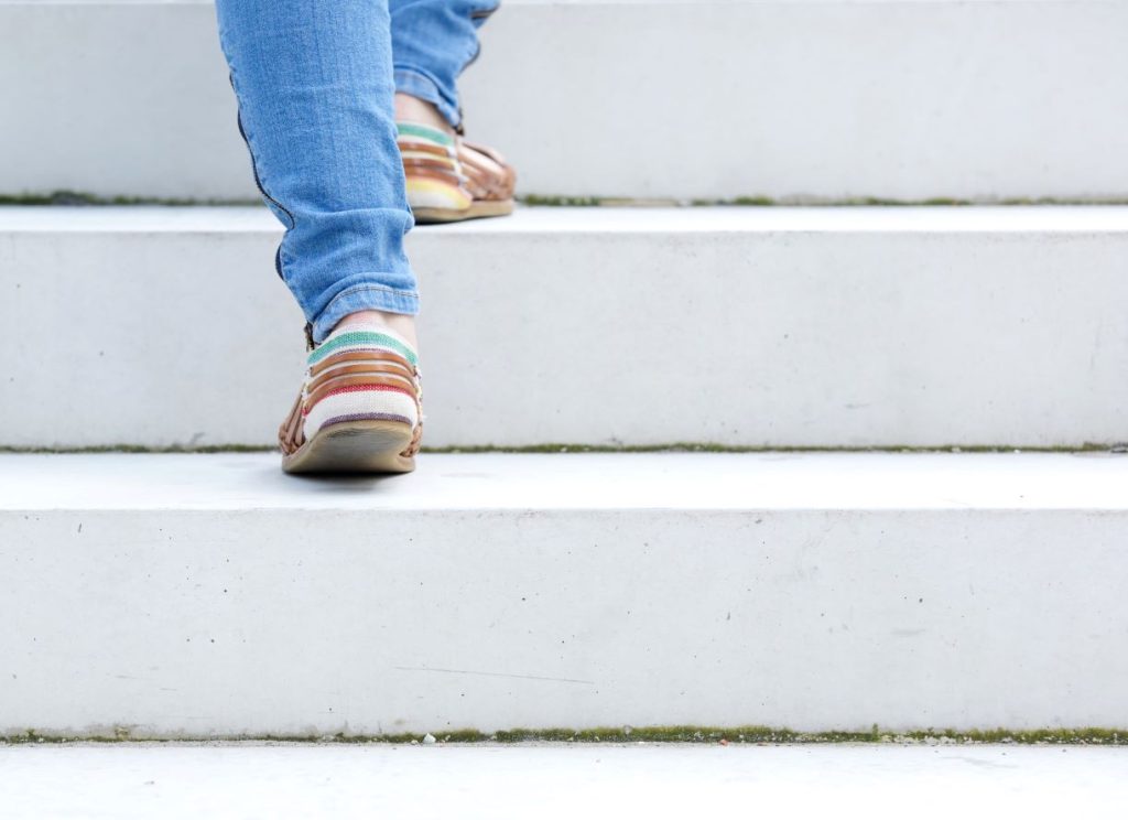 Person wearing blue jeans and colorful striped shoes walking up white concrete steps; photo is focused on their legs and feet.