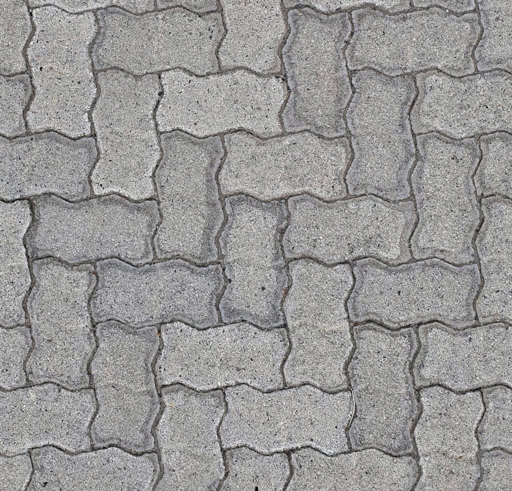 Close-up view of interlocking gray pavers arranged in a repeating, zigzag pattern, creating a textured surface commonly used for sidewalks or home outdoor pathways.