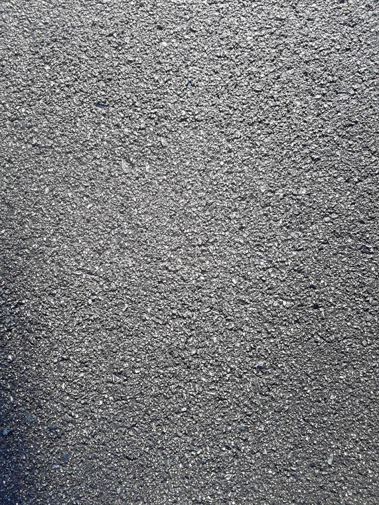 A close-up view of a textured asphalt surface, showing small stones and rough gray material commonly used in road construction.
