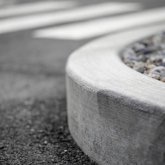 Close-up of a concrete curb beside an asphalt road with small pebbles on one side and a blurred pedestrian crosswalk visible in the background.